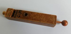 This is a lifesize photo of an all-wooden cuckoo call with a stamp indicating "Frank Wolf Drummers Supplies - NYC". This call was probably manufactured around 1940 to 1955. The wooden ball on the right is connected to a wood rod with a thin wood plate on the inside that can be moved in and out to alter the size of the air space to finely tune the overall pitch of the call. Of course, the higher note of the 2-pitch cuckoo call is produced with the finger hole uncovered. By covering the hole the lower pitch is produced.